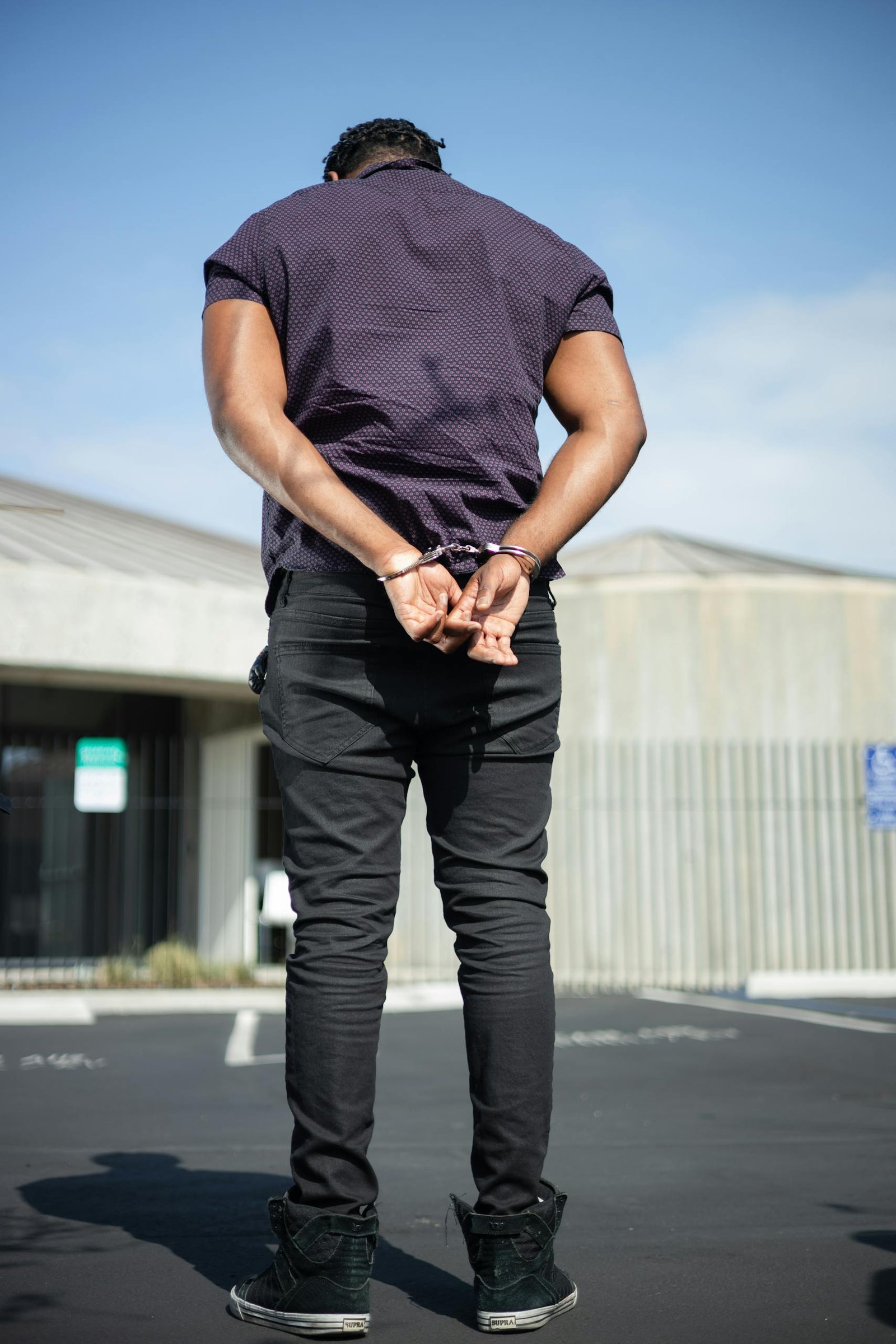 Back view of a man with handcuffs standing outside on a sunny day.