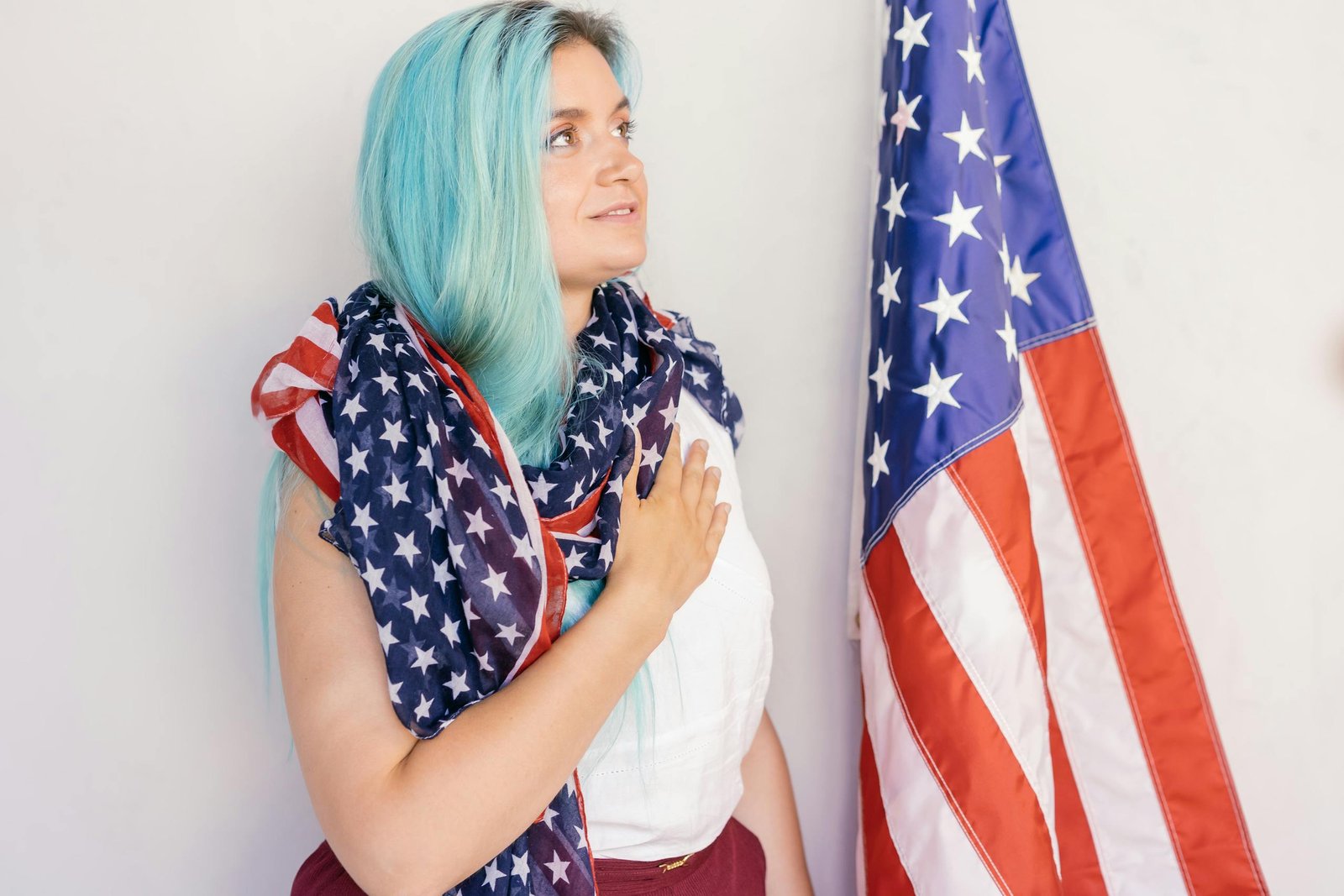 Caucasian woman draped in American flag standing by stars and stripes, showing patriotism.